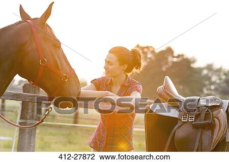 Stock Image - Woman looking at horse at rural pasture fence. Fotosearch