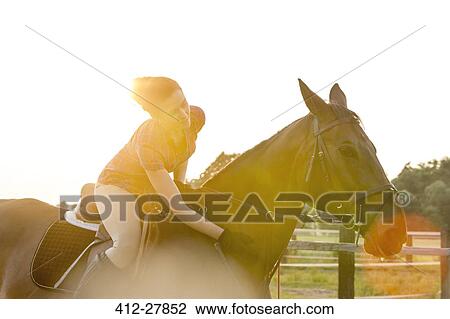 Stock Image - Woman on horseback petting horse in rural pasture. Fotosearch