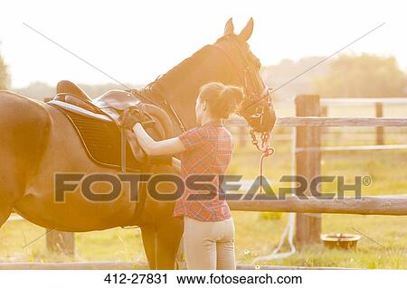 Woman preparing saddle for horseback riding in rural pasture View Large Photo Image Stock Image - Woman preparing saddle for horseback riding in rural pasture. Fotosearch