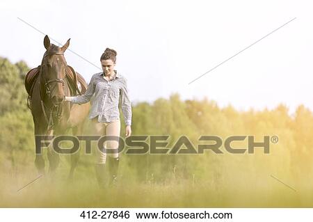 Stock Photograph - Woman walking horse in rural field. Fotosearch