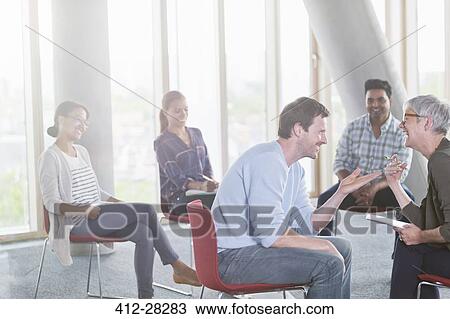 Stock Image - Business people talking and laughing face to face in meeting. Fotosearch