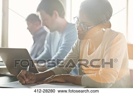 Stock Image - Businesswoman taking notes in meeting. Fotosearch