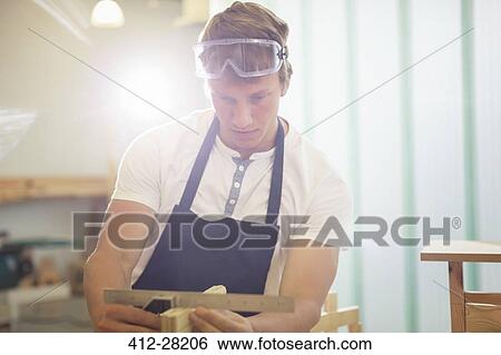 Stock Photograph - Carpenter measuring wood with ruler in workshop. Fotosearch