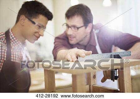 Stock Image - Carpenters measuring wood in workshop. Fotosearch