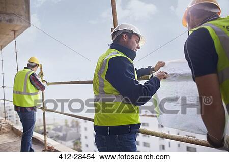Construction worker and engineer reviewing blueprints at highrise construction site View Large Photo Image Picture - Construction worker and engineer reviewing blueprints at highrise construction site. Fotosearch