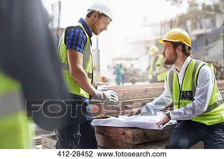 Stock Image - Construction worker and engineer reviewing blueprints at construction site. Fotosearch