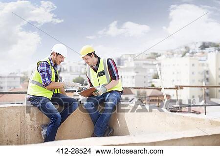 Picture - Construction worker and engineer with clipboard talking at highrise construction site. Fotosearch