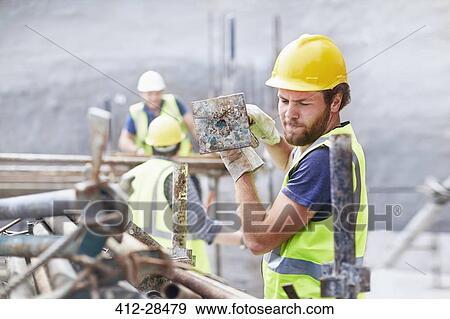Stock Photo - Construction worker carrying metal bar at construction site. Fotosearch