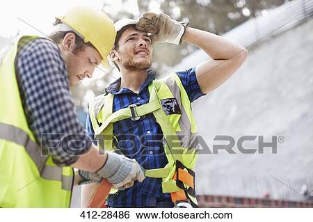 Stock Photograph - Construction worker fastening coworker’s safety harness. Fotosearch