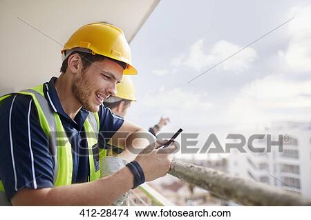 Picture - Construction worker texting at highrise construction site. Fotosearch