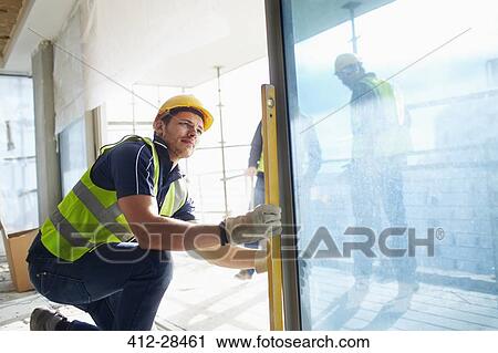 Stock Image - Construction worker using level tool on window at construction site. Fotosearch