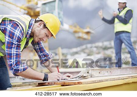 Stock Photo - Construction worker writing on clipboard at construction site. Fotosearch