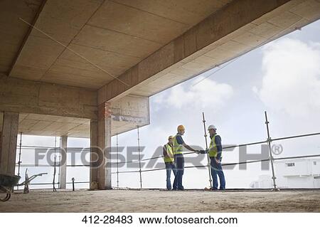 Stock Image - Construction workers handshaking at highrise construction site. Fotosearch