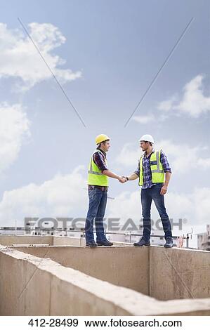 Stock Photo - Construction workers handshaking at highrise construction site. Fotosearch