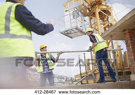 Stock Photo - Construction workers lifting metal pole below crane at construction site. Fotosearch