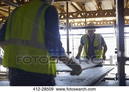 Construction workers lifting plyboard at construction site View Large Photo Image Stock Photo - Construction workers lifting plyboard at construction site. Fotosearch