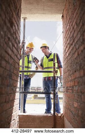 Construction workers texting with cell phone at construction site View Large Photo Image Stock Photo - Construction workers texting with cell phone at construction site. Fotosearch