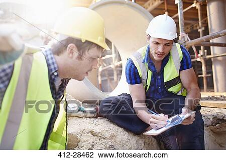 Construction workers with clipboard talking at construction site View Large Photo Image Stock Image - Construction workers with clipboard talking at construction site. Fotosearch