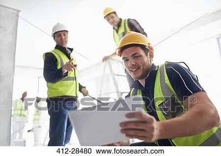 Stock Image - Construction workers with digital tablet at construction site. Fotosearch