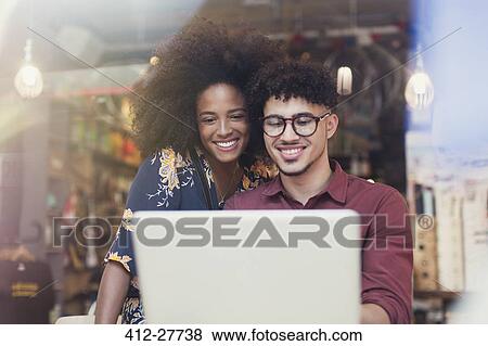 Stock Photo - Couple using laptop at cafe window. Fotosearch