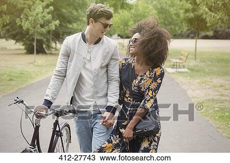 Stock Image - Couple walking with bicycle in park. Fotosearch