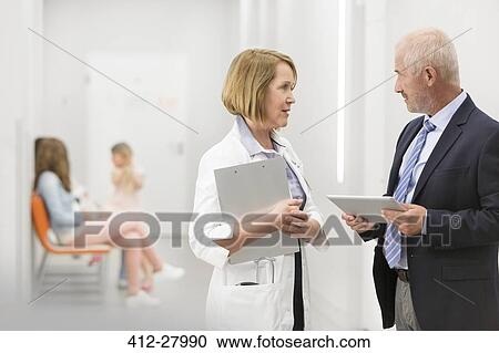 Stock Image - Doctor and administrator with digital tablet talking in hospital corridor. Fotosearch