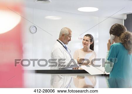 Stock Photograph - Doctor and patient discussing medical record at nurses station. Fotosearch