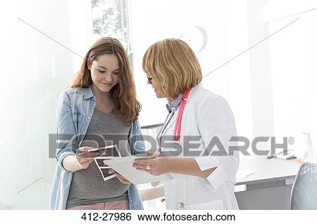 Stock Photograph - Doctor and pregnant teenage patient viewing ultrasound x-rays in doctor’s office. Fotosearch