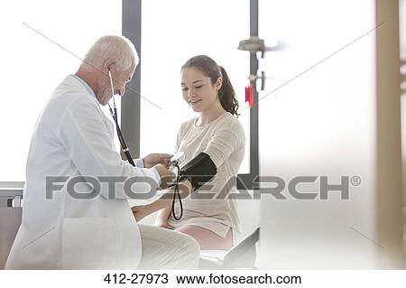 Stock Image - Doctor checking teenage patient’s blood pressure with cuff in examination room . Fotosearch