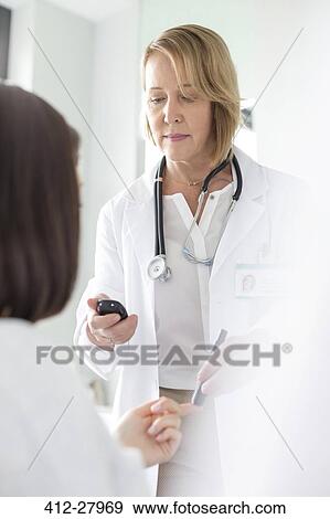 Stock Photo - Doctor testing patient blood sugar for diabetes in examination room. Fotosearch