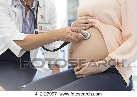 Stock Photo - Doctor using stethoscope on pregnant patient’s stomach. Fotosearch