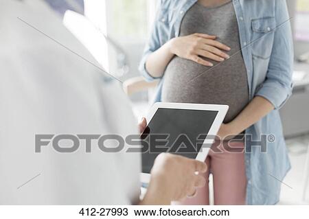 Stock Image - Doctor with digital tablet talking to pregnant patient. Fotosearch