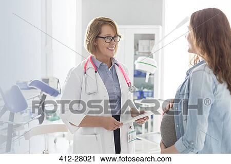 Stock Image - Doctor with digital tablet talking to pregnant patient in examination room. Fotosearch