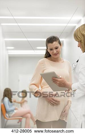Doctor with digital tablet talking to pregnant patient in clinic corridor View Large Photo Image Stock Photography - Doctor with digital tablet talking to pregnant patient in clinic corridor. Fotosearch