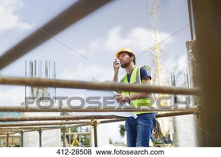 Engineer with blueprints using walkie-talkie at construction site View Large Photo Image Stock Photo - Engineer with blueprints using walkie-talkie at construction site. Fotosearch