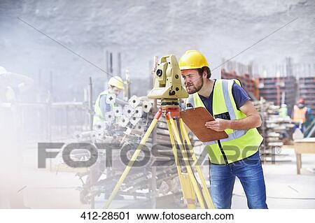 Stock Image - Engineer with clipboard using theodolite at construction site. Fotosearch