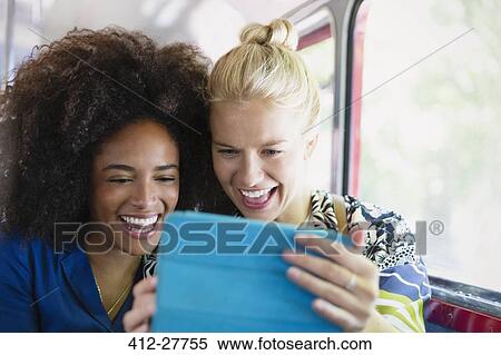 Stock Photography - Enthusiastic friends taking selfie with digital tablet on bus. Fotosearch