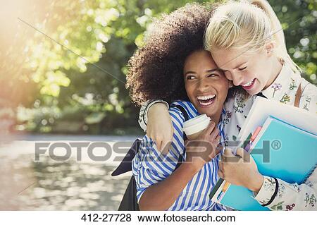 Stock Photo - Enthusiastic friends with books and coffee hugging in park. Fotosearch