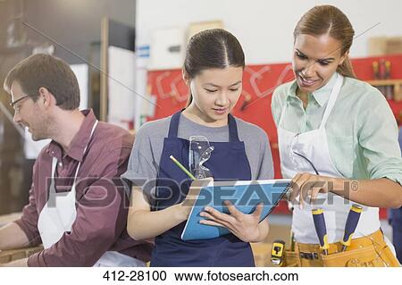 Stock Image - Female carpenters reviewing plans in workshop. Fotosearch
