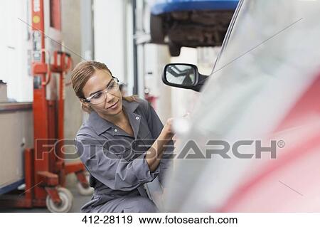 Stock Photo - Female mechanic examining car in auto repair shop. Fotosearch