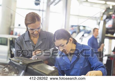 Stock Image - Female mechanics working on engine in auto repair shop. Fotosearch