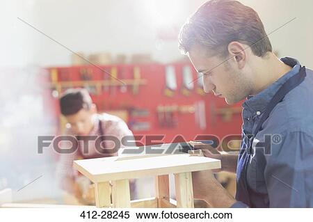 Stock Photography - Focused carpenter measuring wood with ruler in workshop. Fotosearch