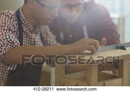 Stock Image - Focused carpenters measuring wood with ruler in workshop. Fotosearch