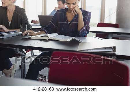 Stock Image - Focused woman studying with textbook in adult education classroom. Fotosearch