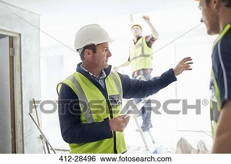 Foreman with digital tablet gesturing to construction worker at construction site View Large Photo Image Stock Photograph - Foreman with digital tablet gesturing to construction worker at construction site. Fotosearch