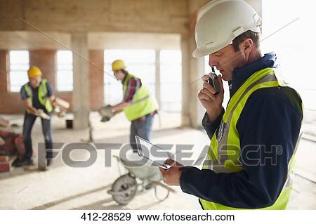 Foreman with digital tablet using walkie-talkie at construction site View Large Photo Image Stock Photo - Foreman with digital tablet using walkie-talkie at construction site. Fotosearch