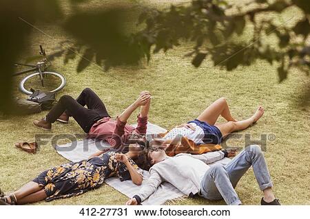 Stock Image - Friends taking selfie laying in circle on blanket in park. Fotosearch