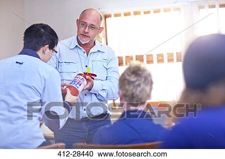Stock Image - Instructor explaining how to use fire extinguisher in training class. Fotosearch