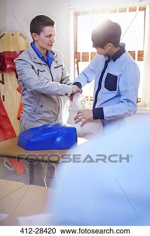 Stock Image - Instructor guiding student with manual resuscitator in CPR training class. Fotosearch