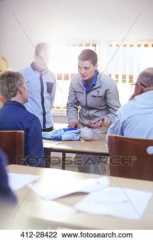 Stock Image - Instructor over CPR dummy leading training class. Fotosearch